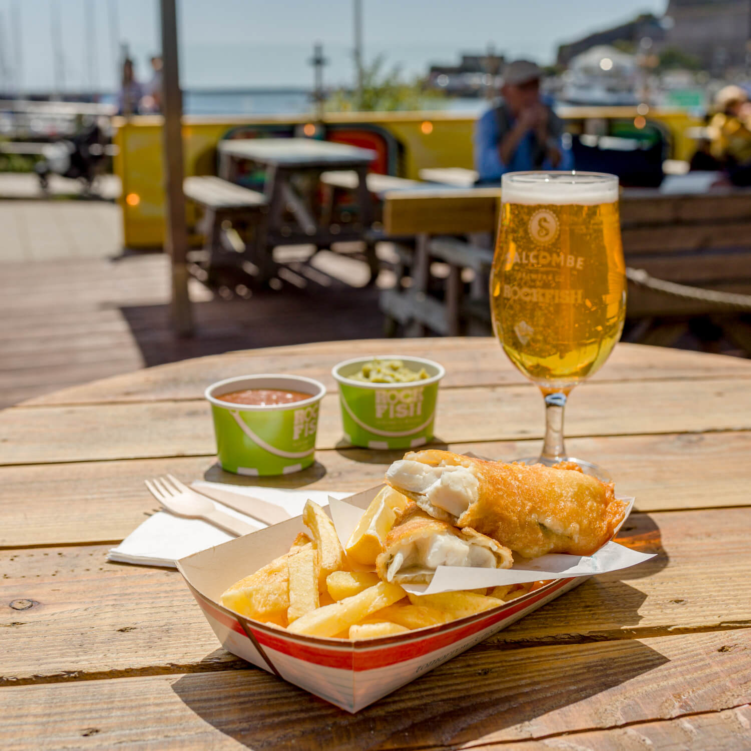 Portion of Rockfish takeaway with sides and a drink on a table outside at Rockfish Plymouth
