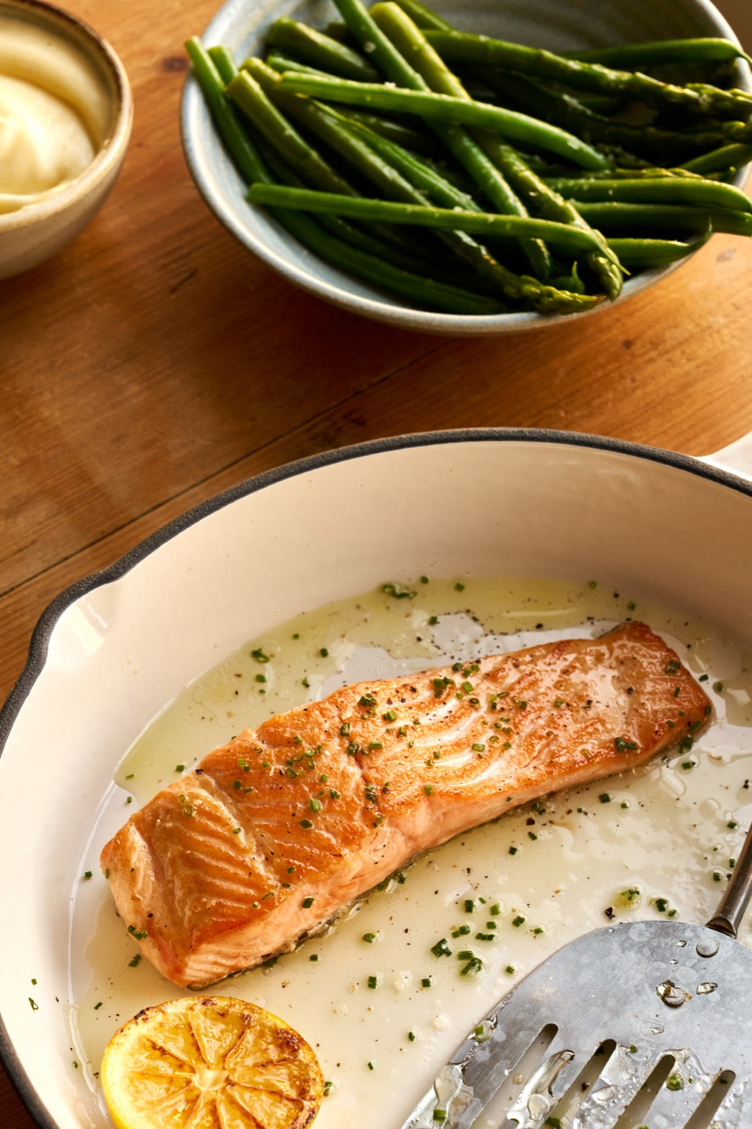 A cooked portion of Chalk Stream Trout in a dish next to some aspargus