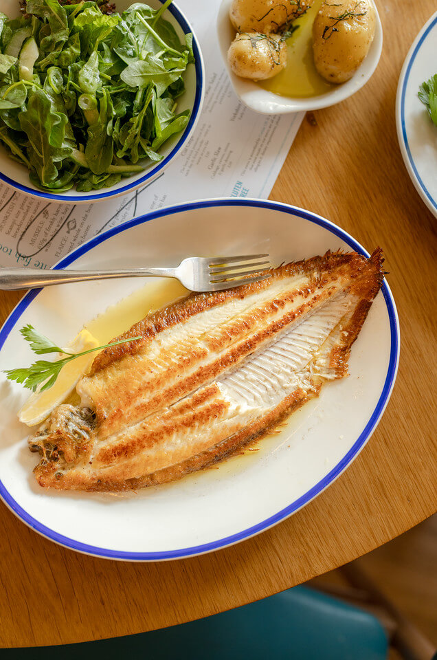Dover Sole from Rockfish on a plate with a piece of the fillet removed. Sits next to a bowl of salad and potatoes