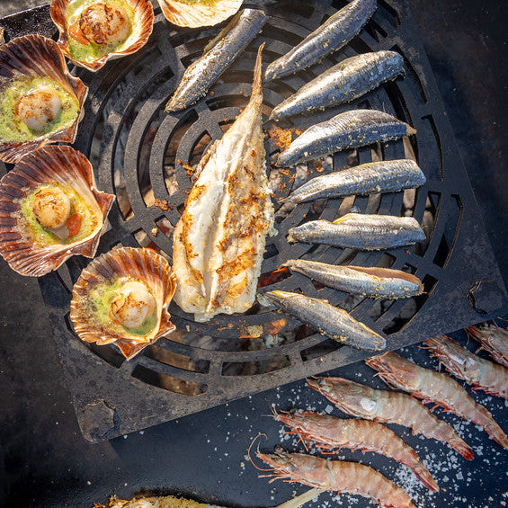 A selection of seafood on a bbq inlcuding wholemonkfish, scallops in the half shell and prawns
