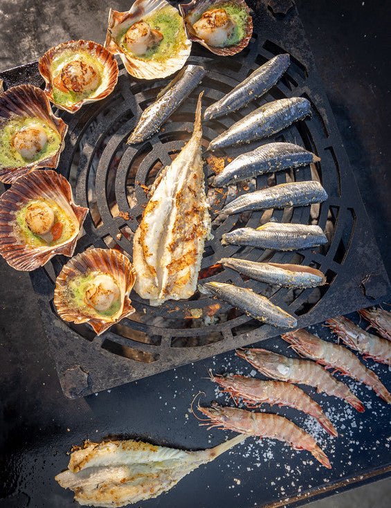 A selection of seafood on a bbq inlcuding wholemonkfish, scallops in the half shell and prawns
