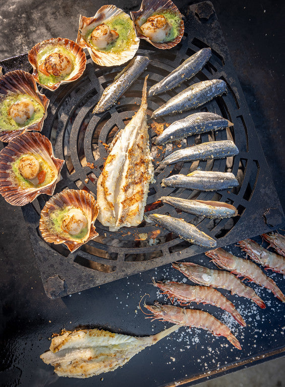 A selection of seafood on a bbq inlcuding wholemonkfish, scallops in the half shell and prawns