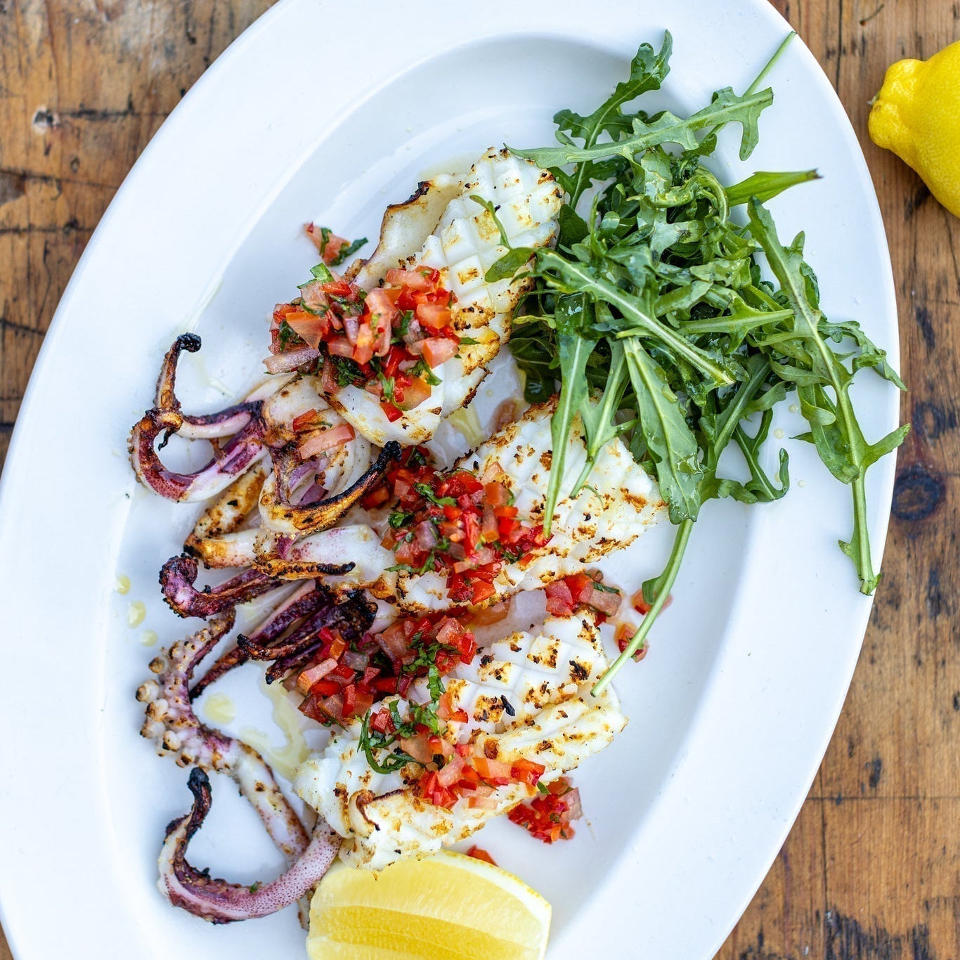 chargrilled squid with fresh pepper dressing and rocket on an oval plate on a wooden table