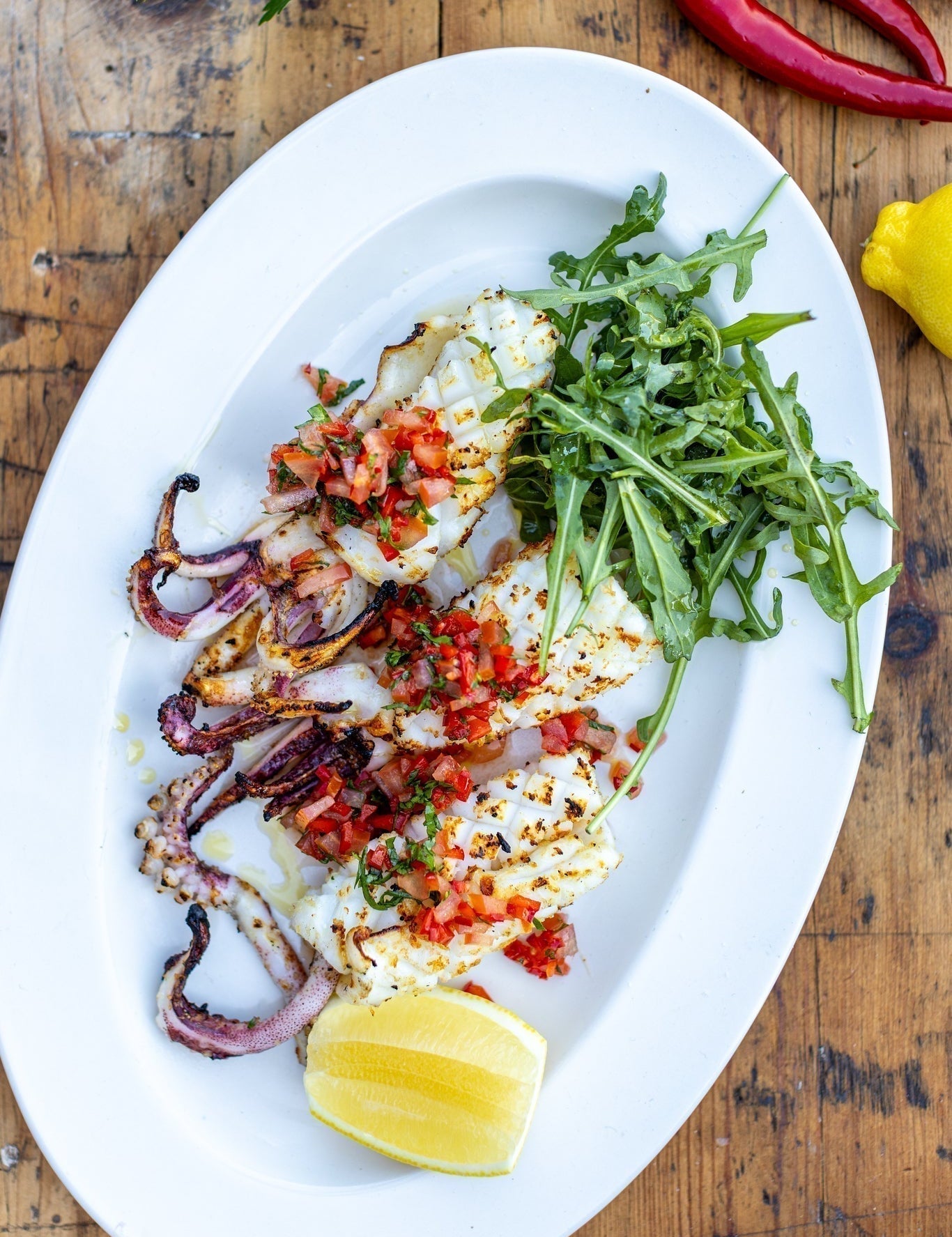 chargrilled squid with fresh pepper dressing and rocket on an oval plate on a wooden table