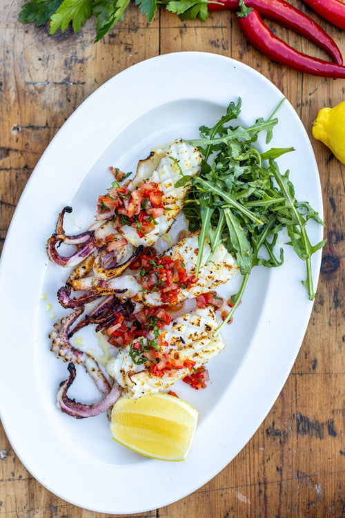 chargrilled squid with fresh pepper dressing and rocket on an oval plate on a wooden table