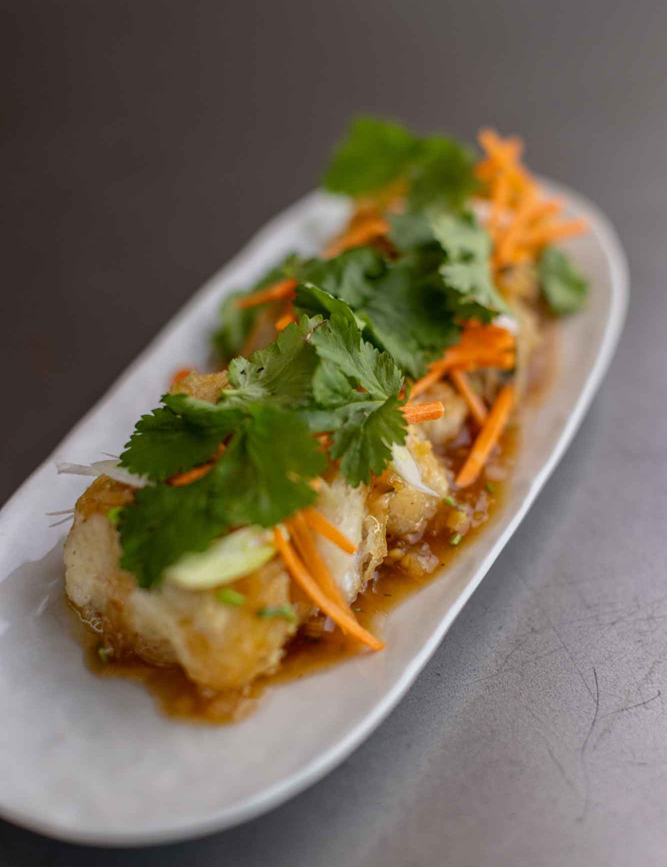 Fried monkfish cheeks with a sauce. Garnished with carrot and coriander