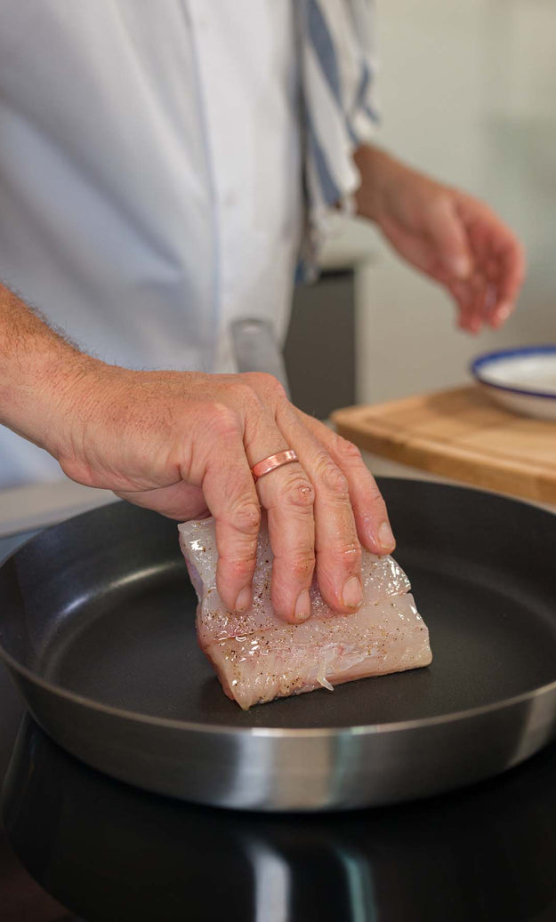 A fresh piece of Hake being placed into a frying pan
