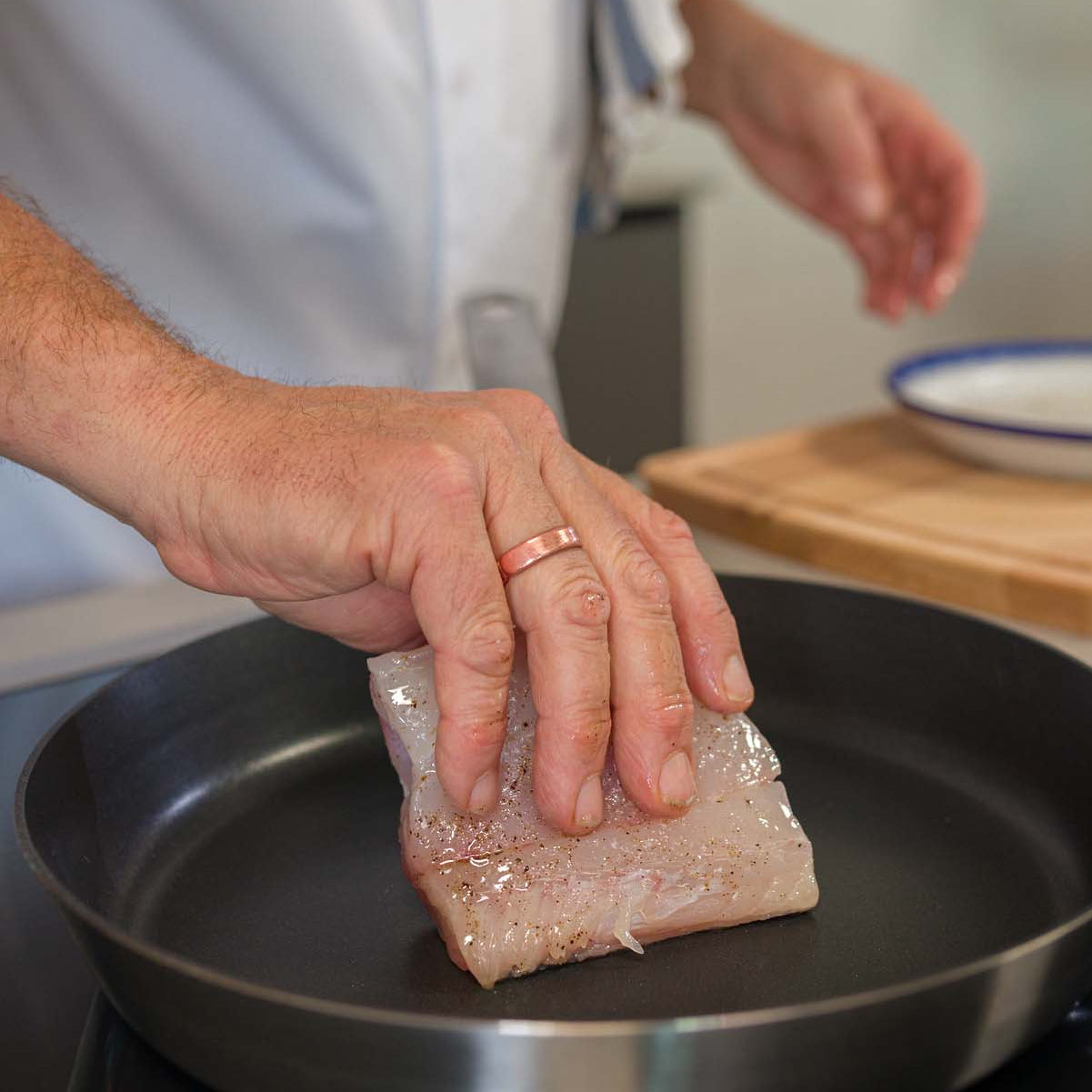 A fresh piece of Hake being placed into a frying pan