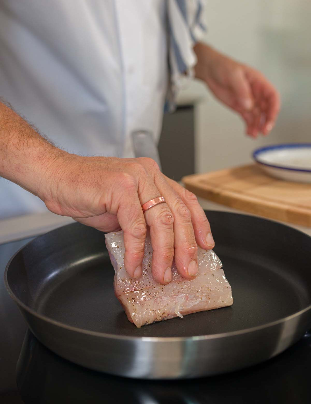 A fresh piece of Hake being placed into a frying pan