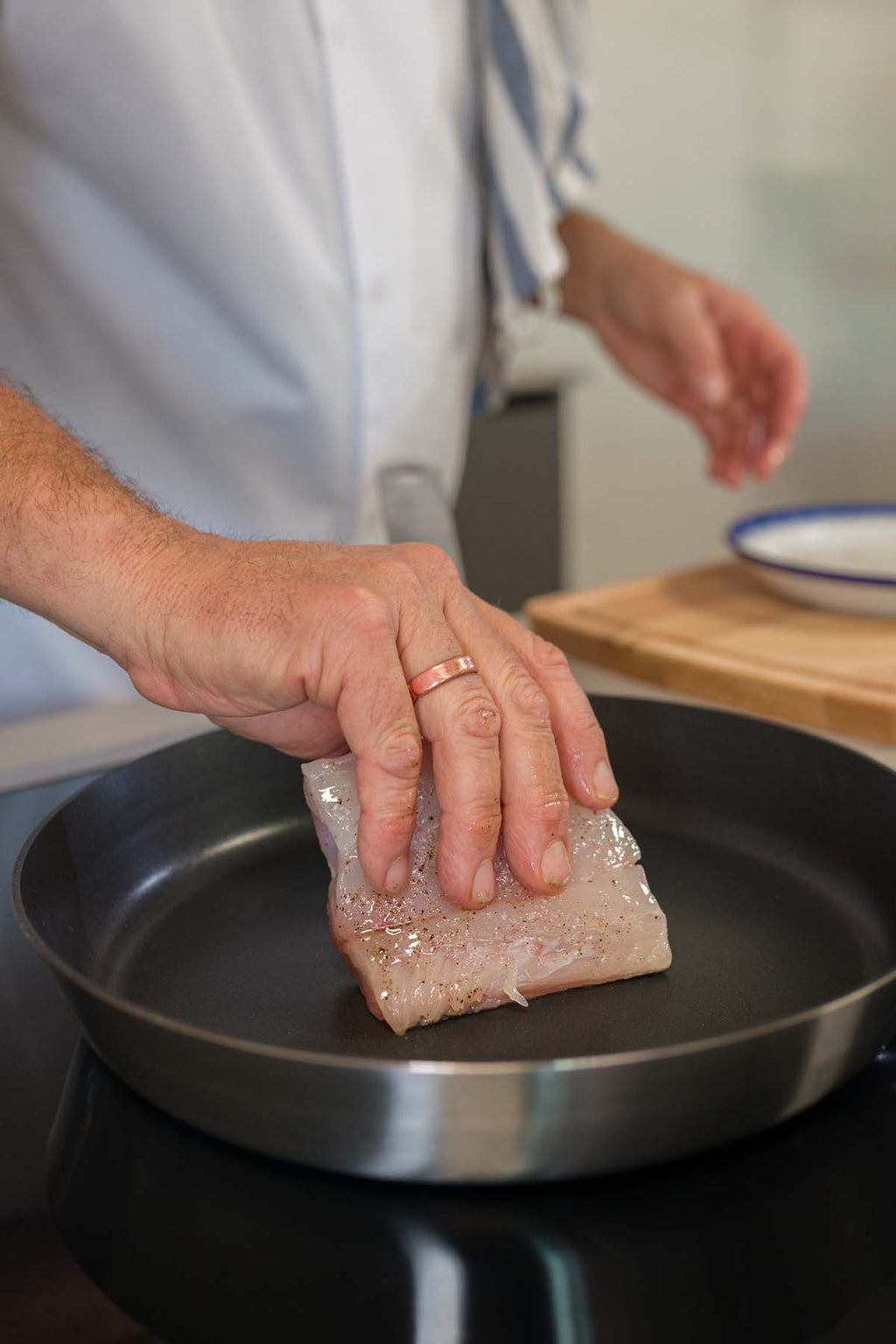 A fresh piece of Hake being placed into a frying pan