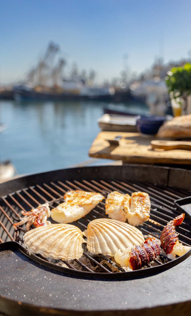 Seafood including scallops, lobster tail, squid and monkfish being cooked on a bbq at Brixham quayside