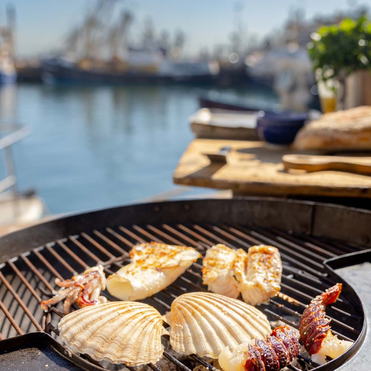 Seafood including scallops, lobster tail, squid and monkfish being cooked on a bbq at Brixham quayside