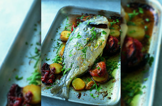 Whole roasted Sea Bream on tray with roasted potatoes and tomatoes