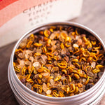 A close-up of a round silver tin filled with citrusy tincture mix from Stony Groves, with the branded box blurred in the background on a wooden surface.