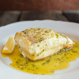Turbot T-bone cooked and sitting in butter with a wedge of lemon to the side.