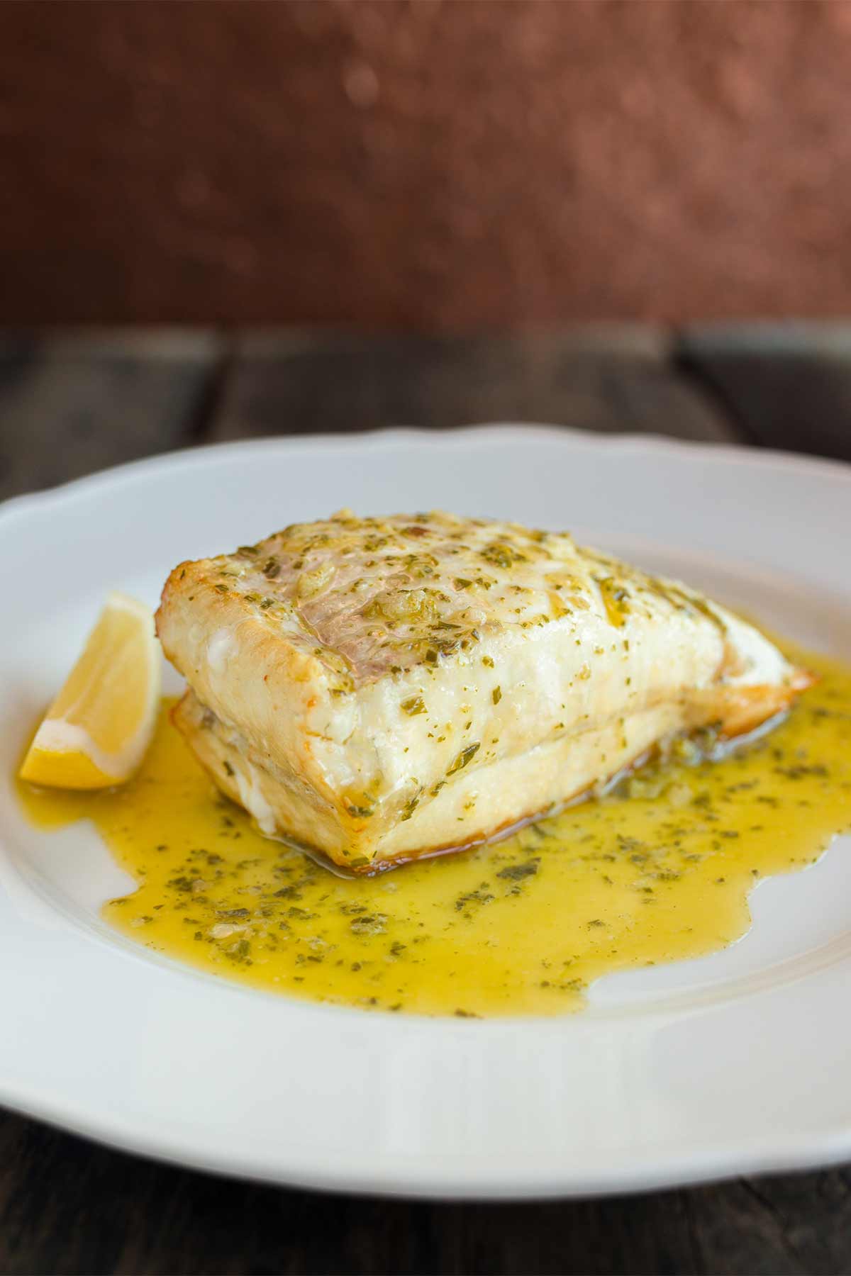 Turbot T-bone cooked and sitting in butter with a wedge of lemon to the side.