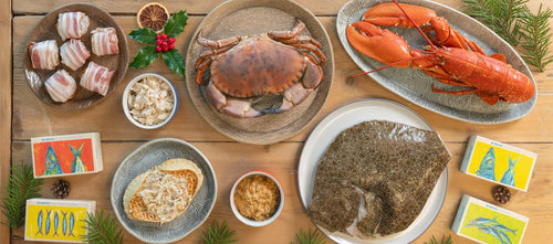 Christmas seafood at Rockfish - scallops wrapped in bacon on a plate, hand picked crab meat in bowls, a whole crab on a plate, a whole lobster on a plate and a prepared whole turbot 
