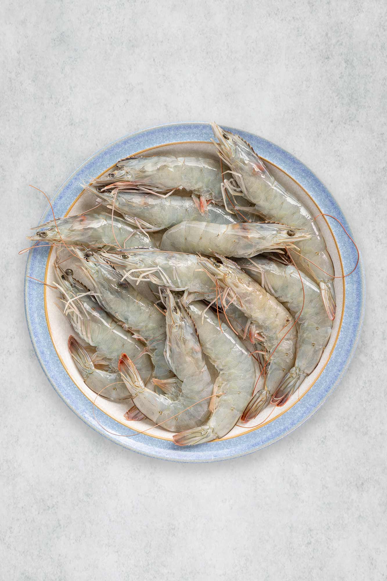 Raw prawns on a round plate with a light gray background