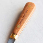 A close-up of a Dorset Oysters knife with a polished wooden handle engraved with the brand name, set against a light gray background.