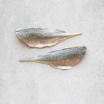 Two horse mackerel fish fillets with silvery-gray skin and pale beige undersides, arranged horizontally on a light gray textured surface.