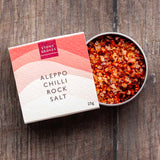 Aleppo Chilli rock salt open pot sitting half in its cardboard packaging on a wooden background. 