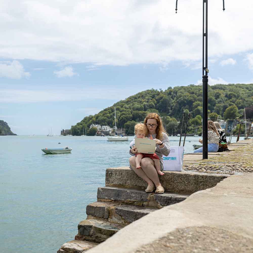 Woman & child enjoying a Rockfish fish & chips at the edge of the water in Dartmouth