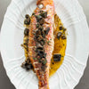 A cooked whole Red Mullet on a oval plate with pickled walnuts and butter sauce
