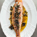 A cooked whole Red Mullet on a oval plate with pickled walnuts and butter sauce