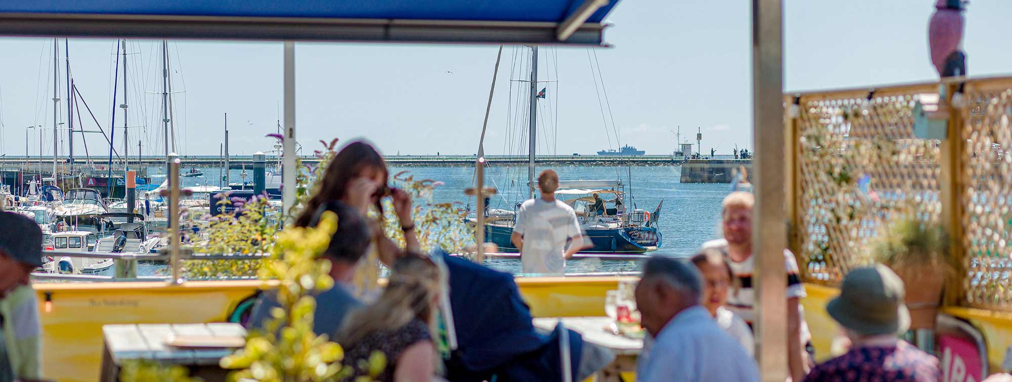 the view of sailing boats from Rockfish Plymouth takeaway. People enjoying fish and chips outside on the covered seating 