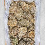 A pack of fresh oysters displayed in a rectangular wooden container they are delivered in.