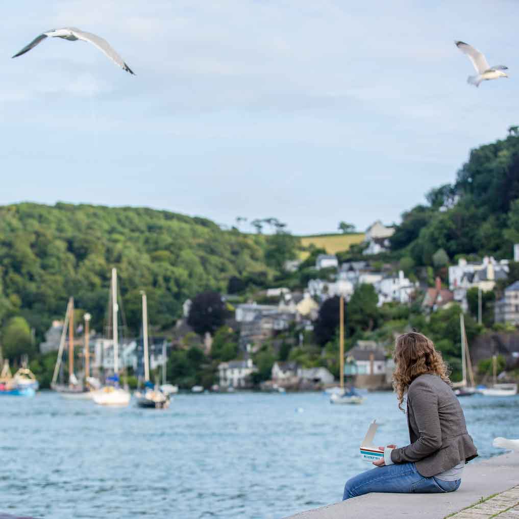 Woman enjoying a Rockfish takeaway by the edge of the water in Dartmouth