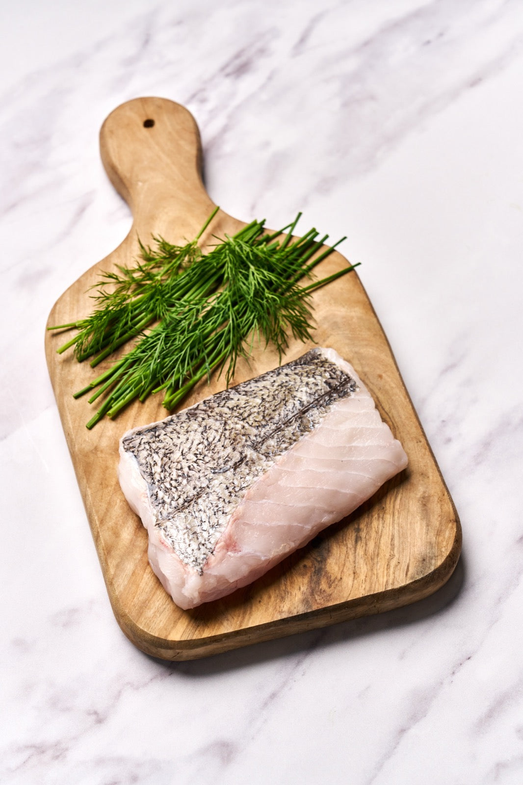A portion of Hake fillet from Rockfish Online Seafood Market on a wooden board