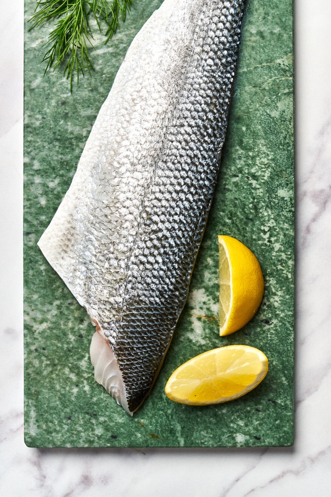 A portion of Sea Bass fillet skin side up from Rockfish Online Seafood Market on a piece of marble.