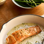A cooked portion of Chalk Stream Trout in a dish next to some aspargus