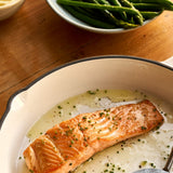 A cooked portion of Chalk Stream Trout in a dish next to some aspargus