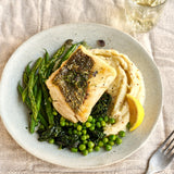 A portion of Hake fillet from Rockfish Online Seafood Market cooked on  plate with a side of mash and some greens.