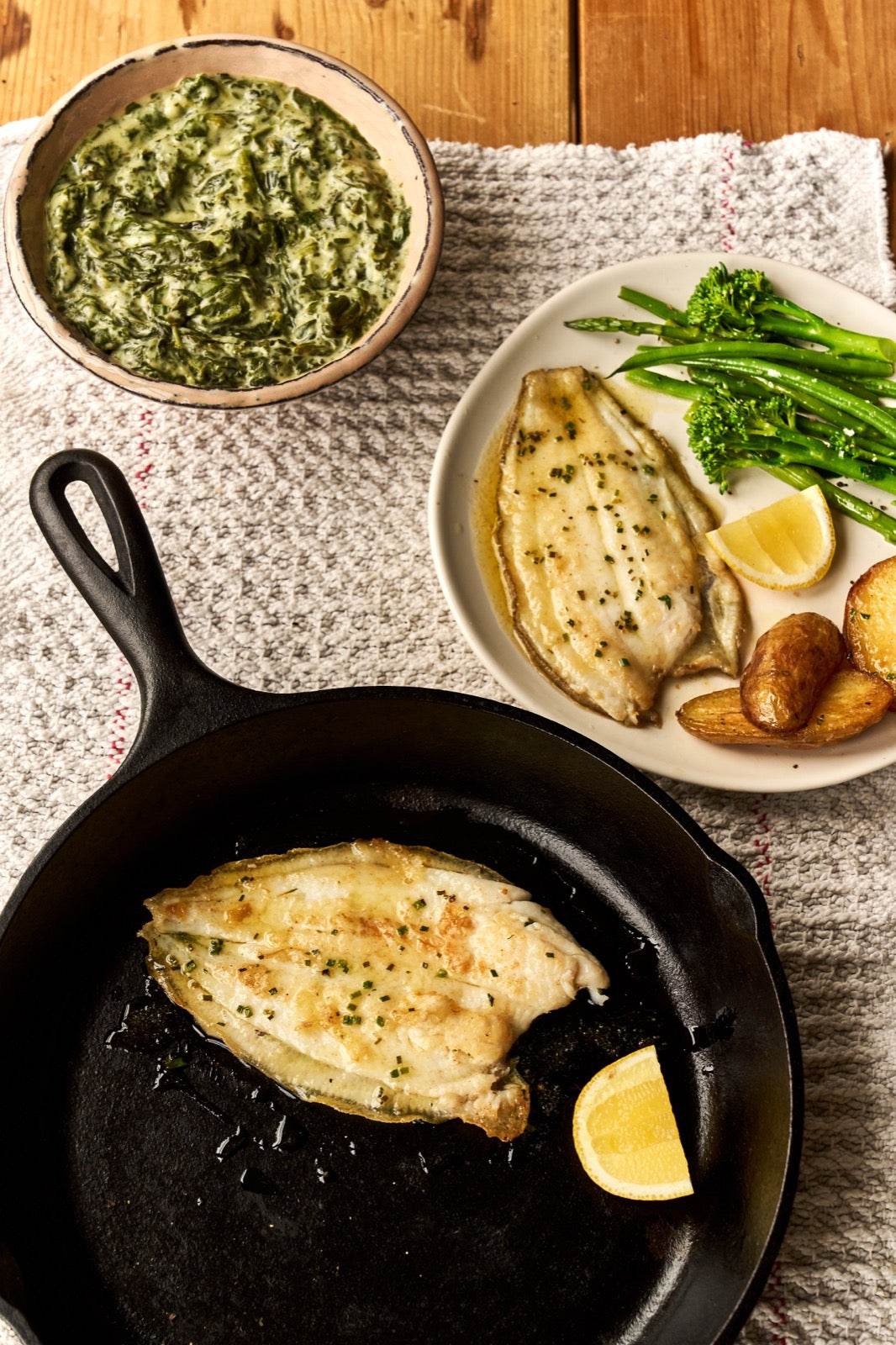 A portion of Lemon Sole fillets from Rockfish Online Seafood Market in a cast iron skillet and on a plate next to it with potato and greens.