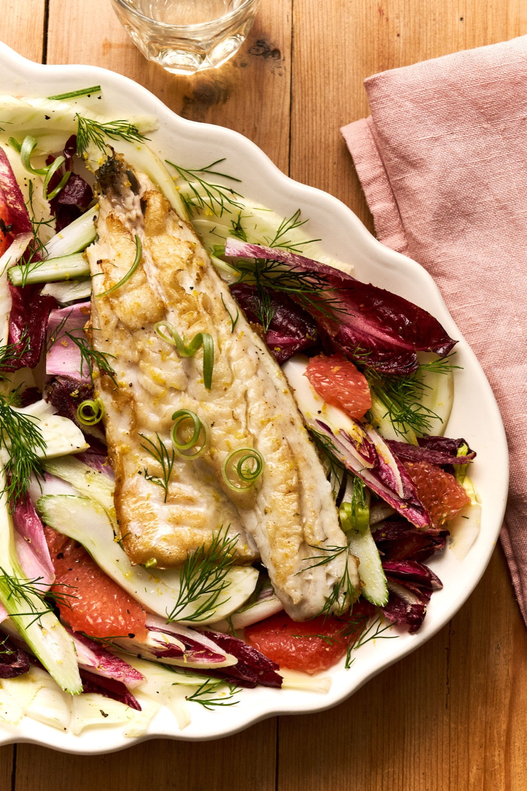 A portion of Seabass fillet from Rockfish Online Seafood Market cooked and nestled on a fresh slaad