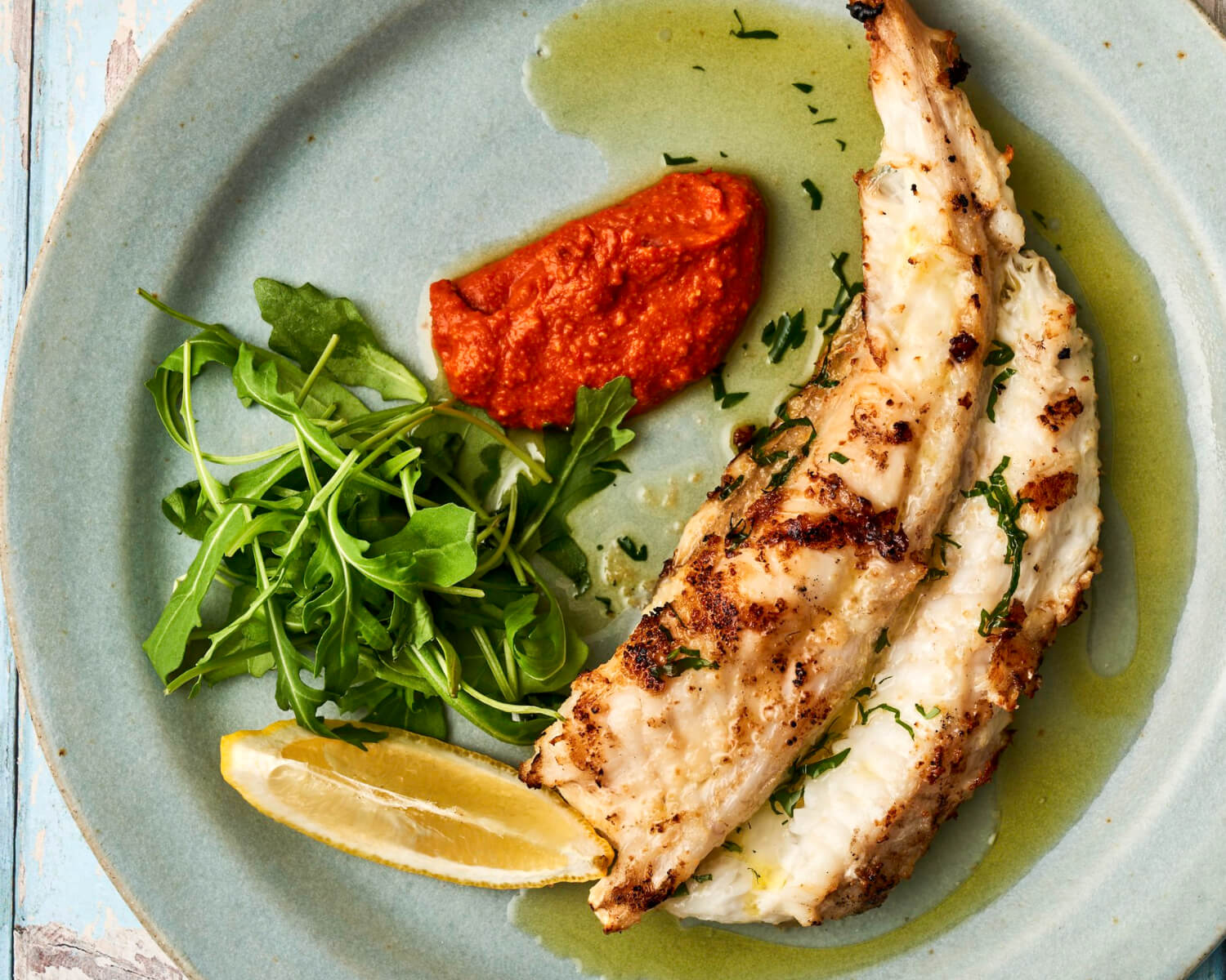 A cooked portion of monkfish tail cooked on a plate with salad and romesco sauce