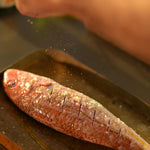 A whole red mullet being prepared on a baking tray