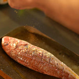 A whole red mullet being prepared on a baking tray