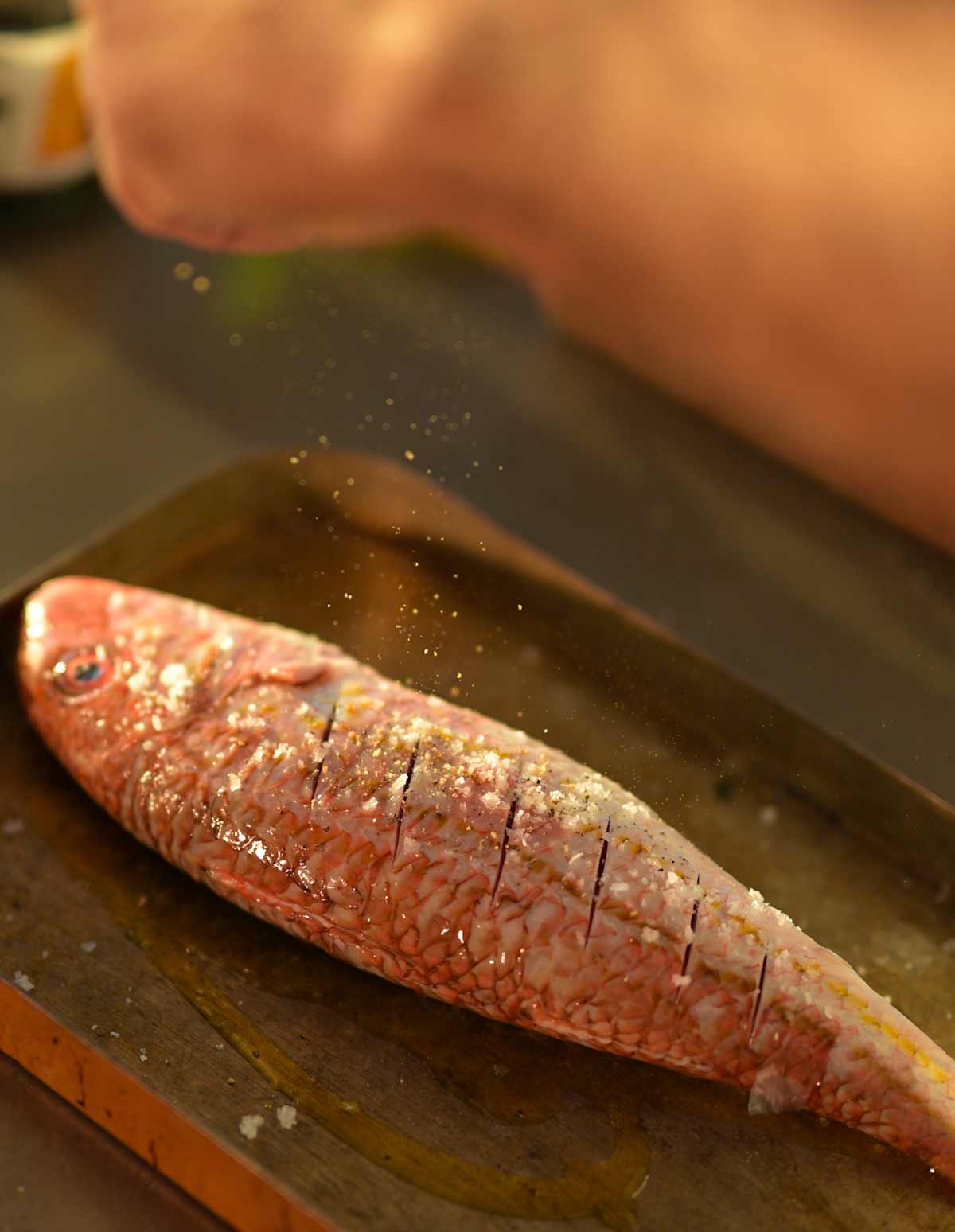 A whole red mullet being prepared on a baking tray