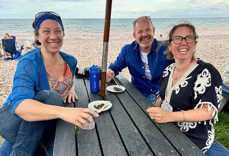 Group of happy people sat on a bench enjoying fresh seafood from Rockfish seafood café in Budleigh