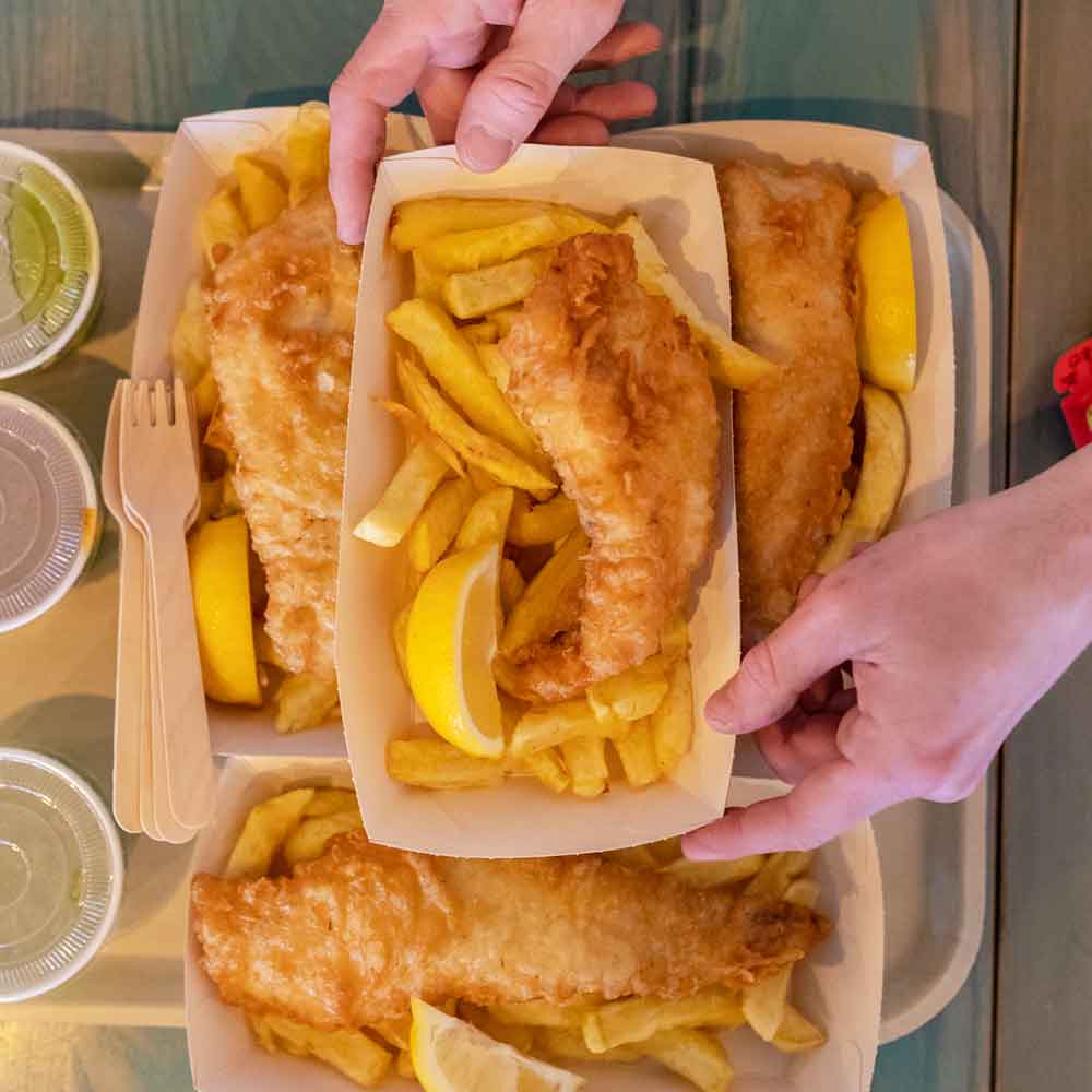 Rockfish takeaway fish & chip portions with wedges of lemon being added to a tray